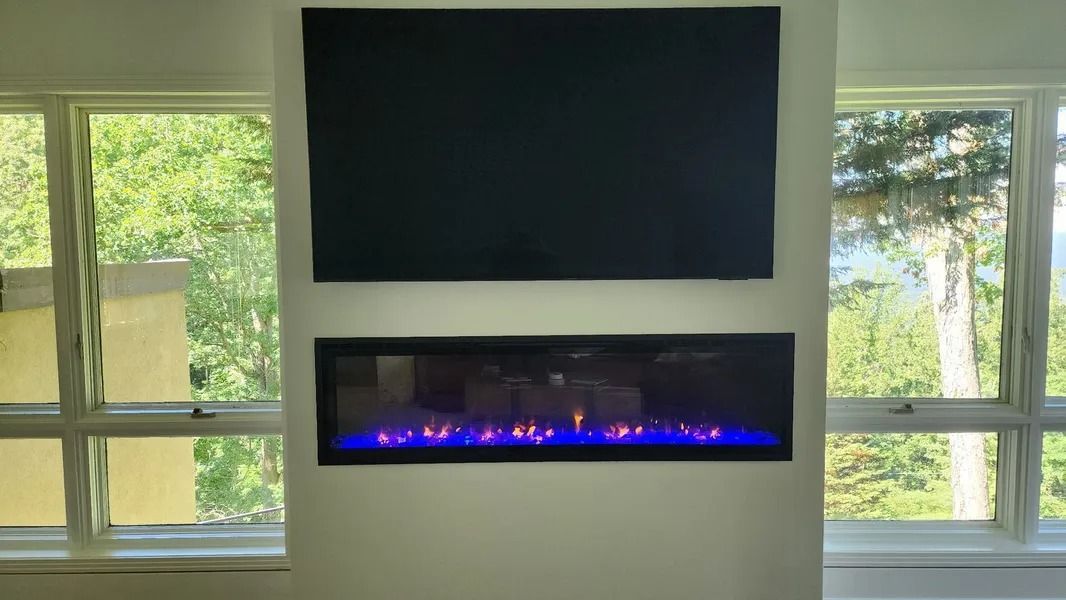 Electric fireplace with blue flames below a mounted black screen, between two windows.