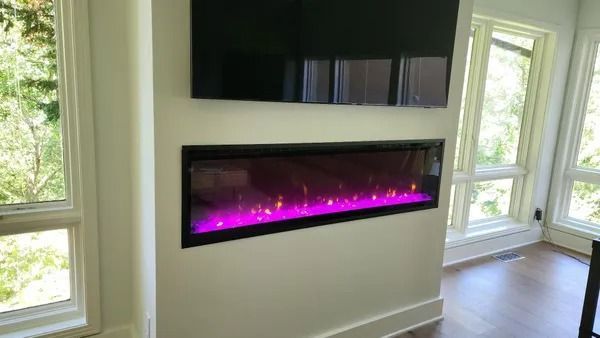 A wall-mounted TV above a rectangular electric fireplace with purple flames, between windows.