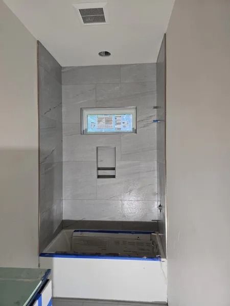Bathroom with gray tiled walls, a window, and a recessed niche. Bathtub below.