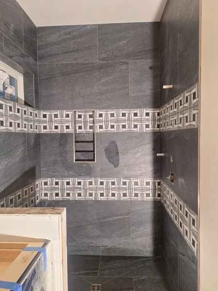 Dark gray tiled shower with decorative border, built-in shelf, and faucet fixtures.