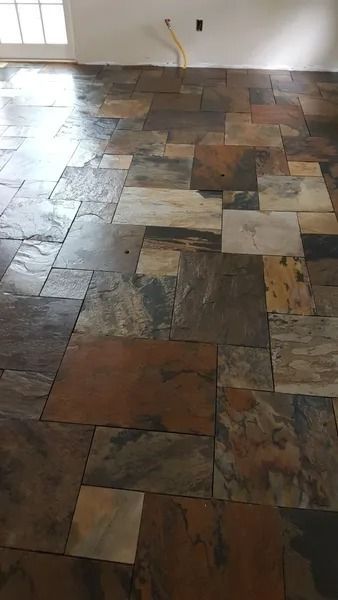 Slate tile flooring with varying colors and textures fills a room, reflecting light.