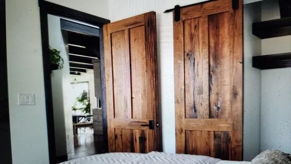 Rustic wooden barn doors in a bedroom, one open to a hallway, the other closed.