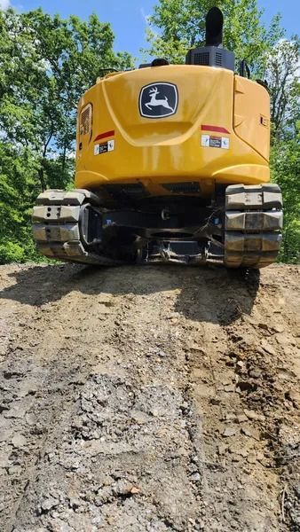 Yellow John Deere excavator on a dirt mound.
