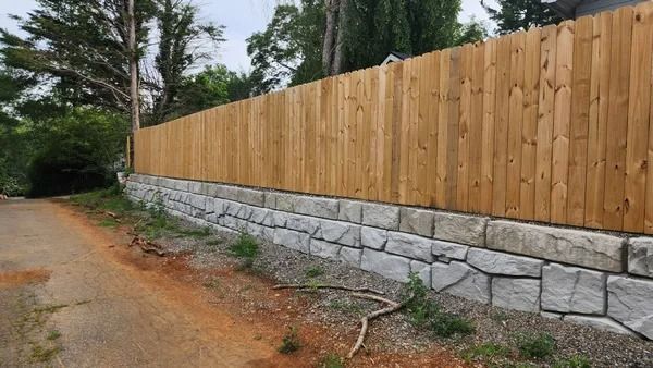 Wooden fence atop a stone retaining wall along a dirt road.