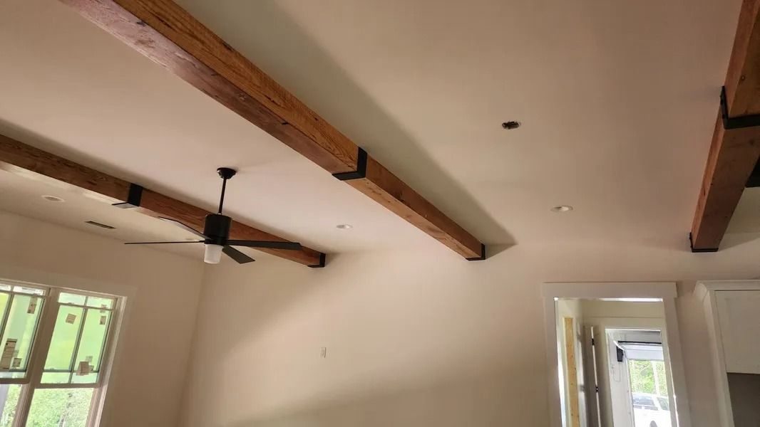 Wooden ceiling beams with black metal supports, white walls, and a ceiling fan in a room.