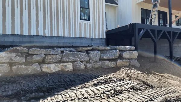 Stone retaining wall beside a building with vertical siding, construction site.