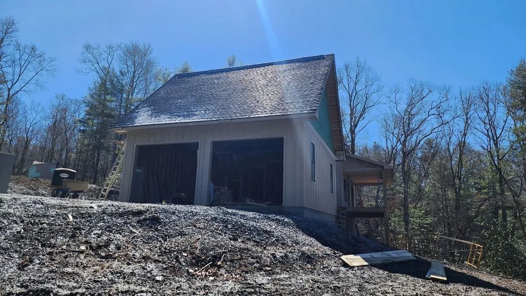 Garage under construction with a weathered roof, surrounded by trees under a blue sky.