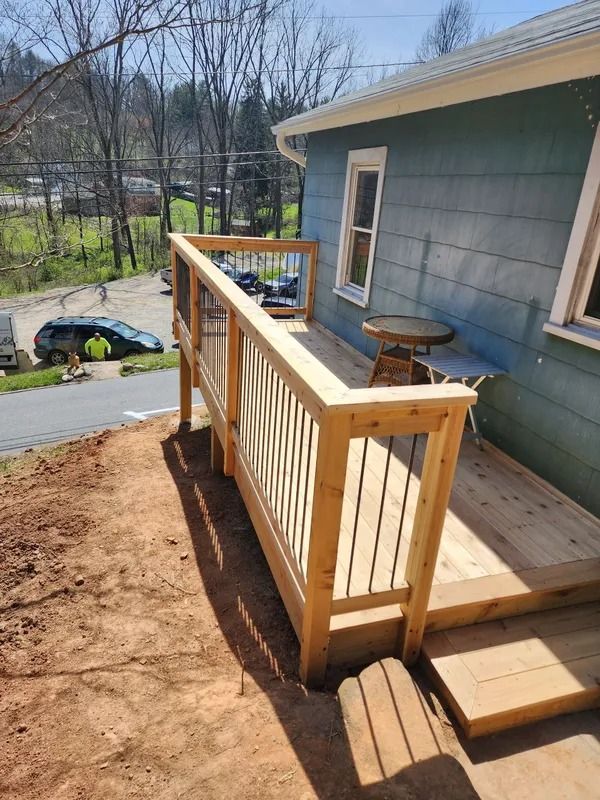Wooden deck with railing, attached to a teal house. Steps lead down to the ground.