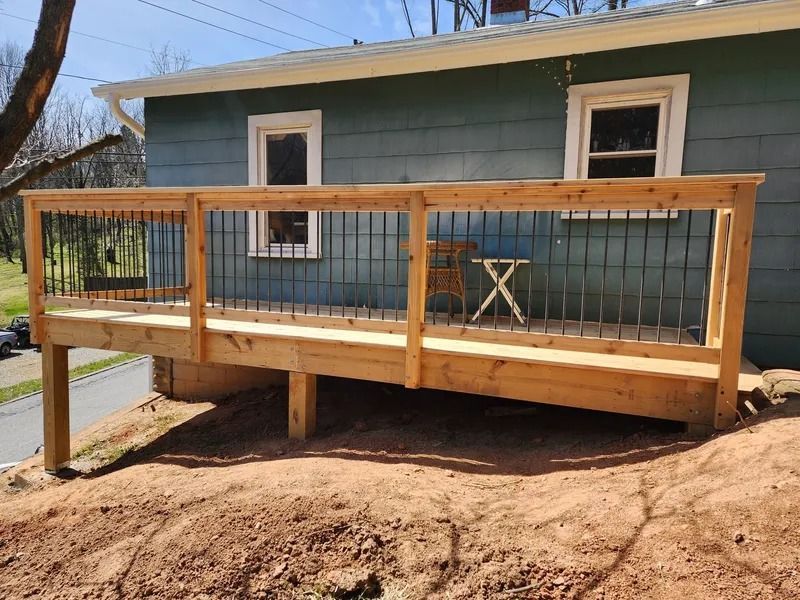 Newly built wooden deck with black railing in front of a green house.