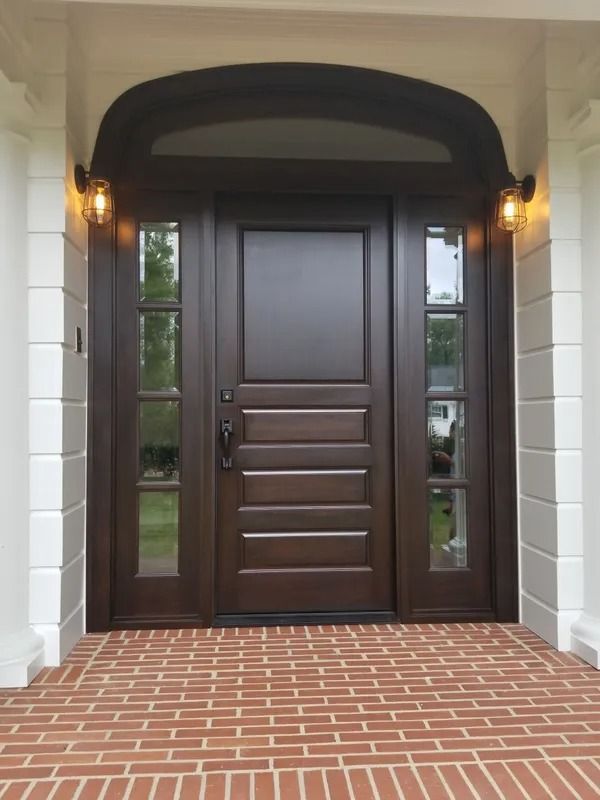 Dark brown front door with sidelights, brick path, and arched white trim.