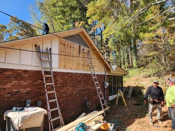 Workers installing siding on a brick house; two ladders and tools are visible.