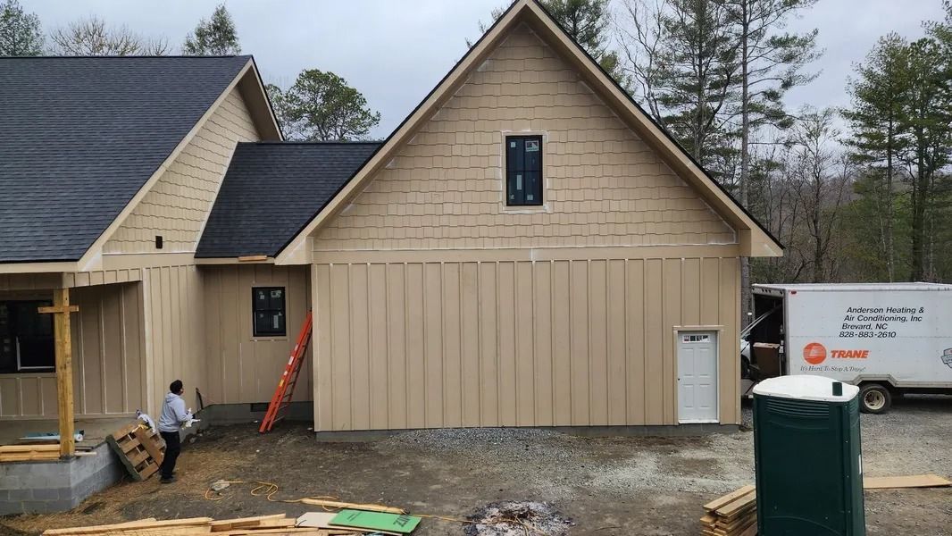 Construction of a tan-sided house with a black roof, a person, and a delivery truck.