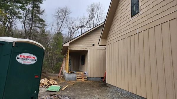 Construction site with a partially built house, portable toilet, and lumber.