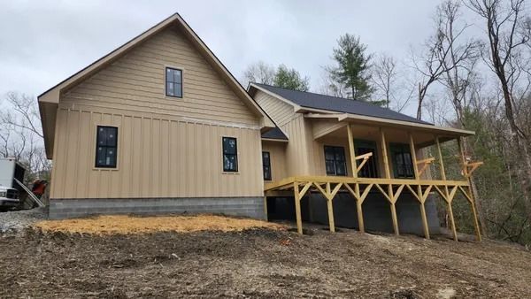 New house under construction with light brown siding, black windows, and a wooden porch.