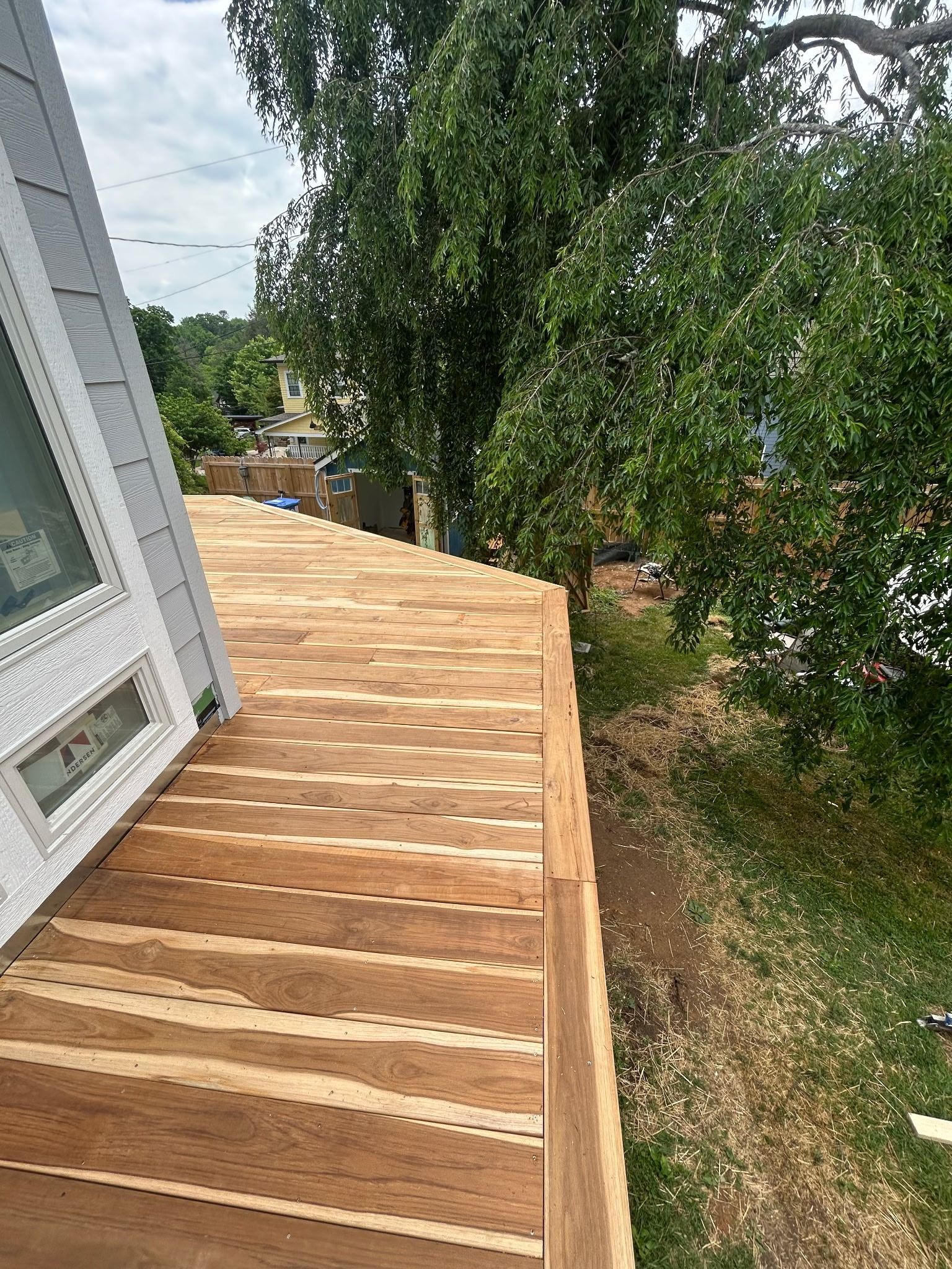 Wooden roof decking beside a white building, with tall trees and a yard below.