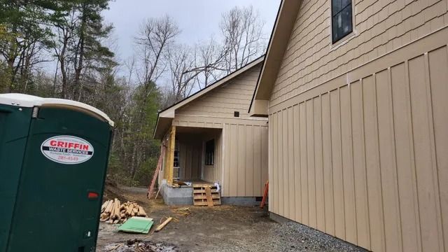 Construction site with a portable toilet and building exterior with tan siding.