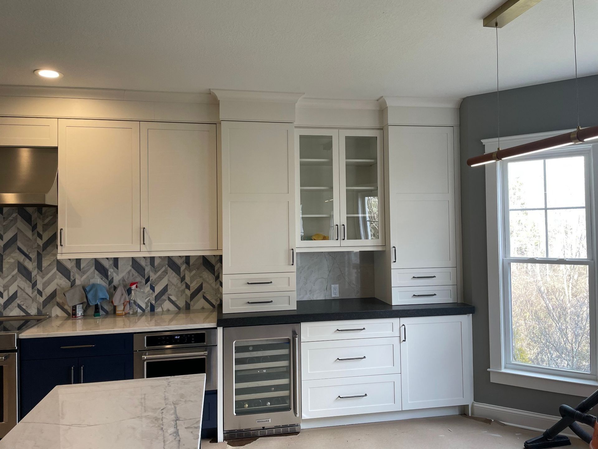 Kitchen with white cabinets, dark countertops, built-in wine cooler, and a window.