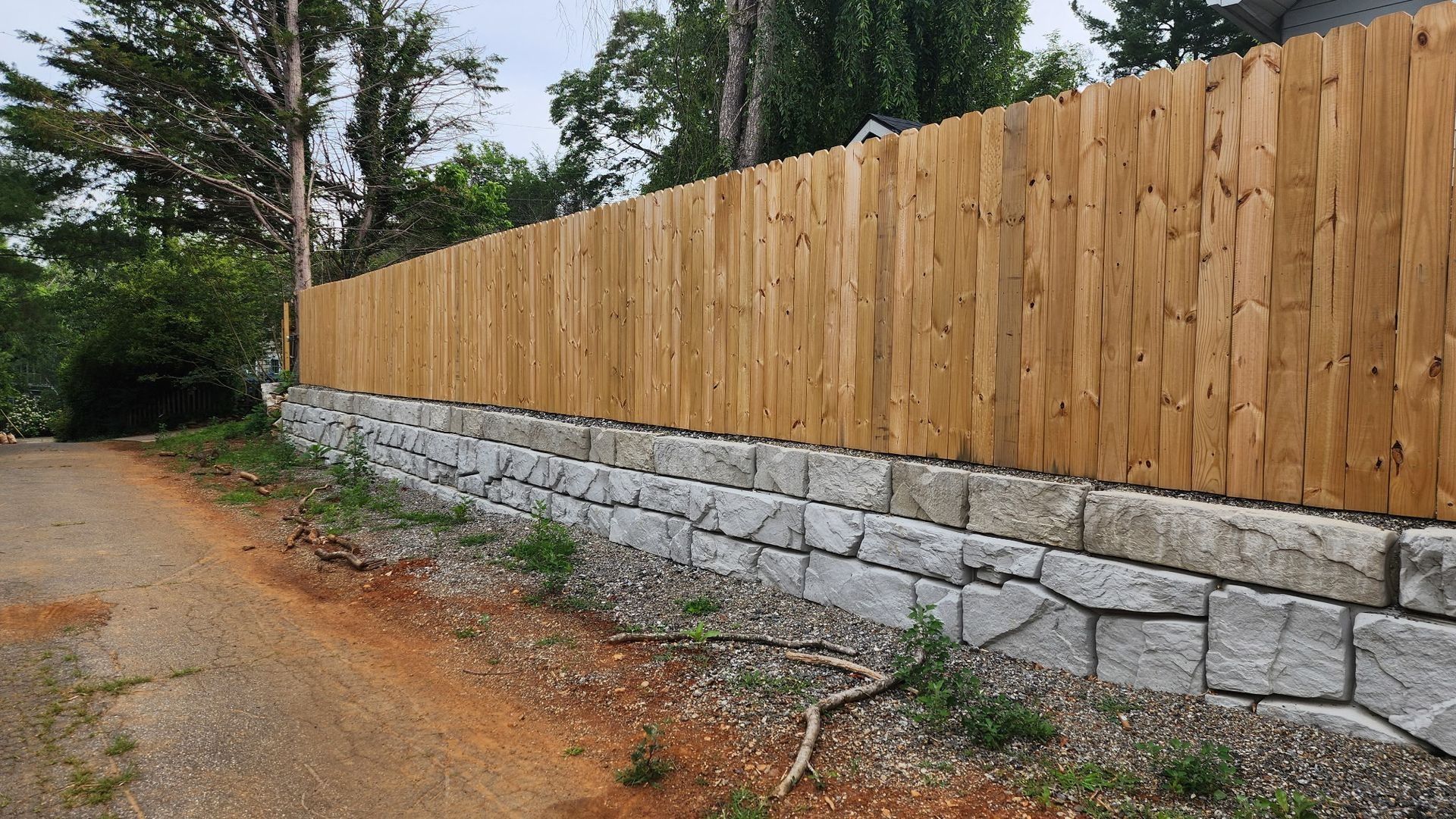 Wooden fence atop a stone retaining wall beside a dirt road.