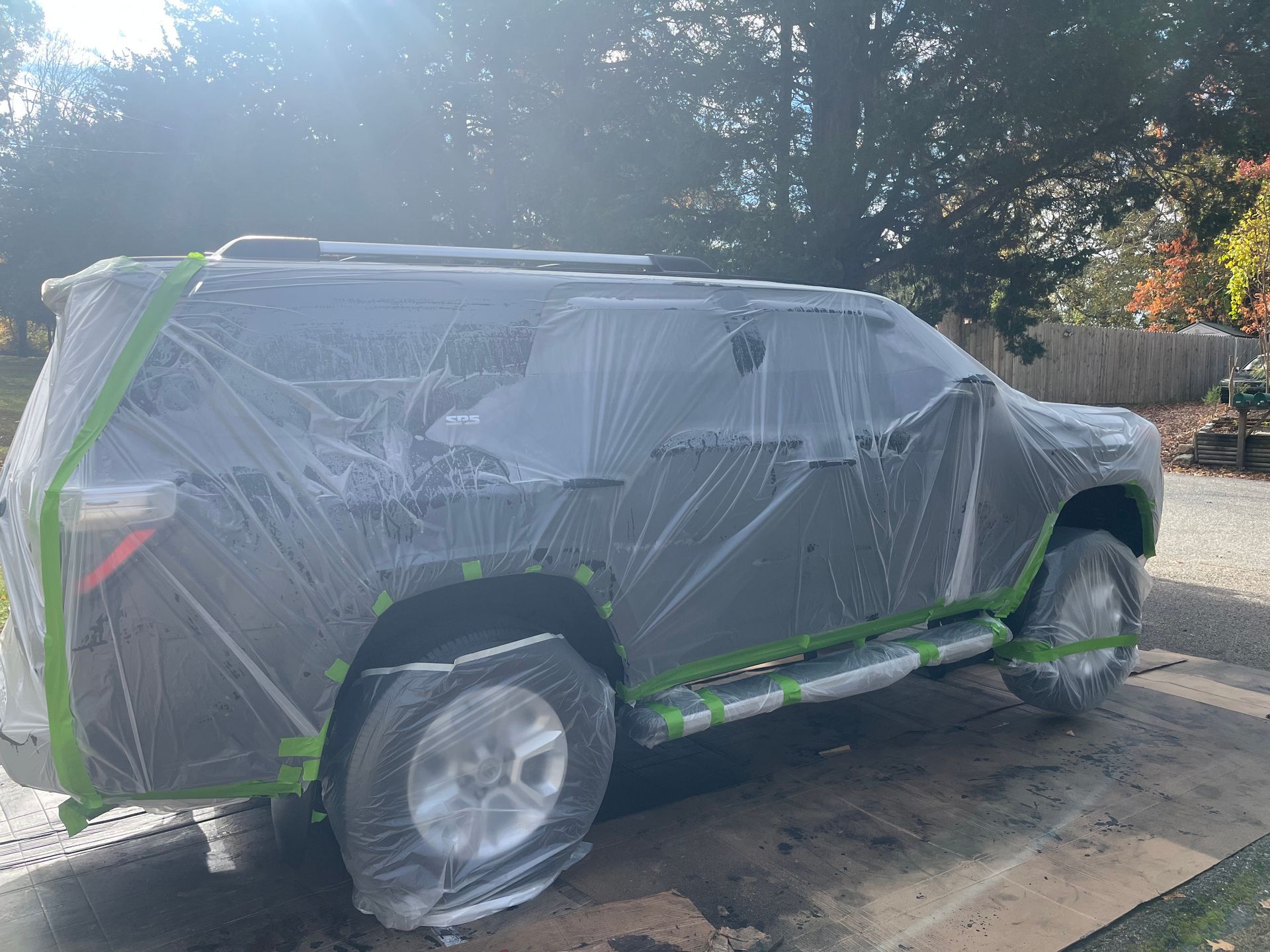 SUV covered in plastic and green tape, possibly for painting, outdoors.