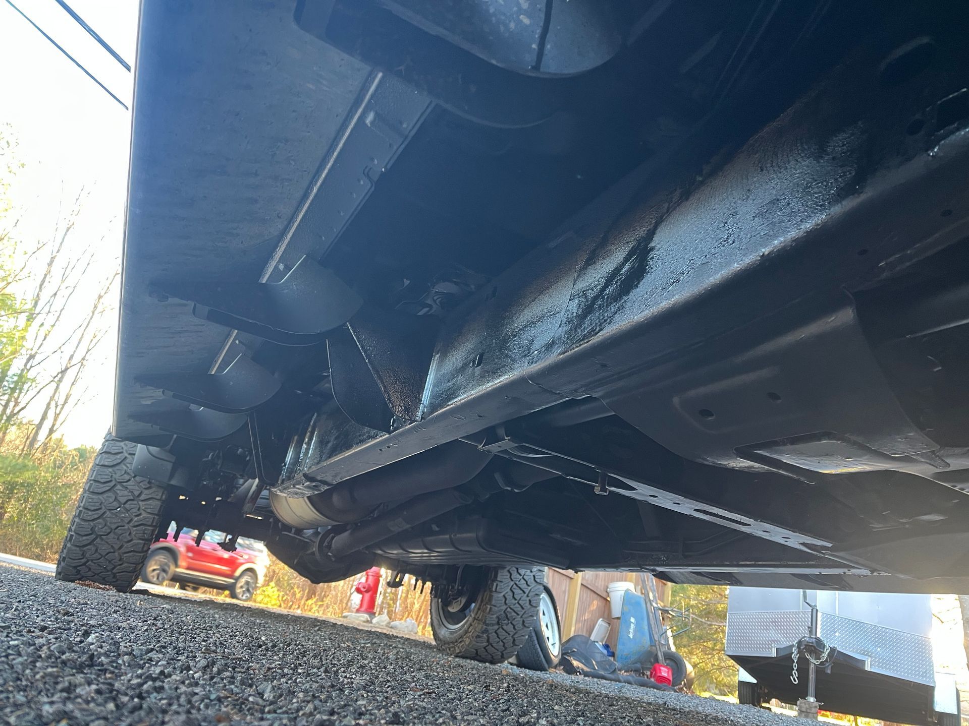 Underside of a black vehicle, coated with what appears to be a protective spray, parked on asphalt.