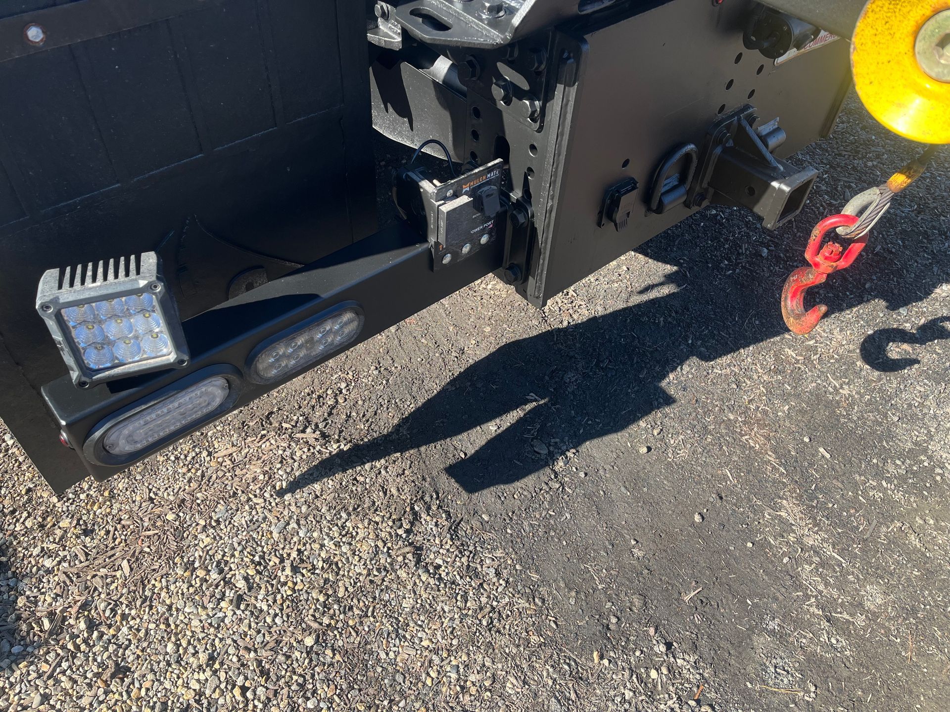 Black tow truck bumper with lights, tow hooks, and a chain on asphalt.