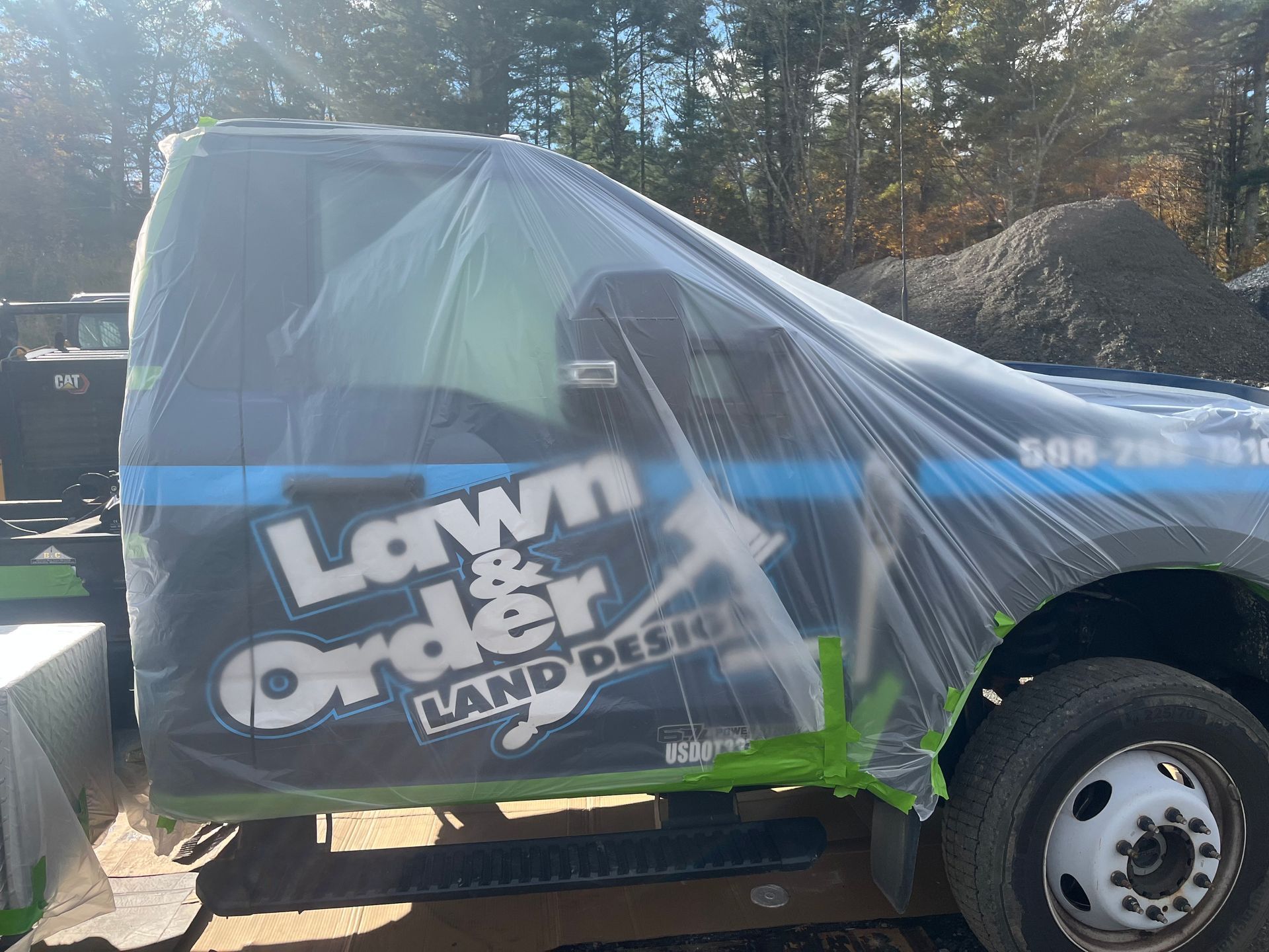 Underside view of a dark vehicle with suspension components visible, parked on gravel.