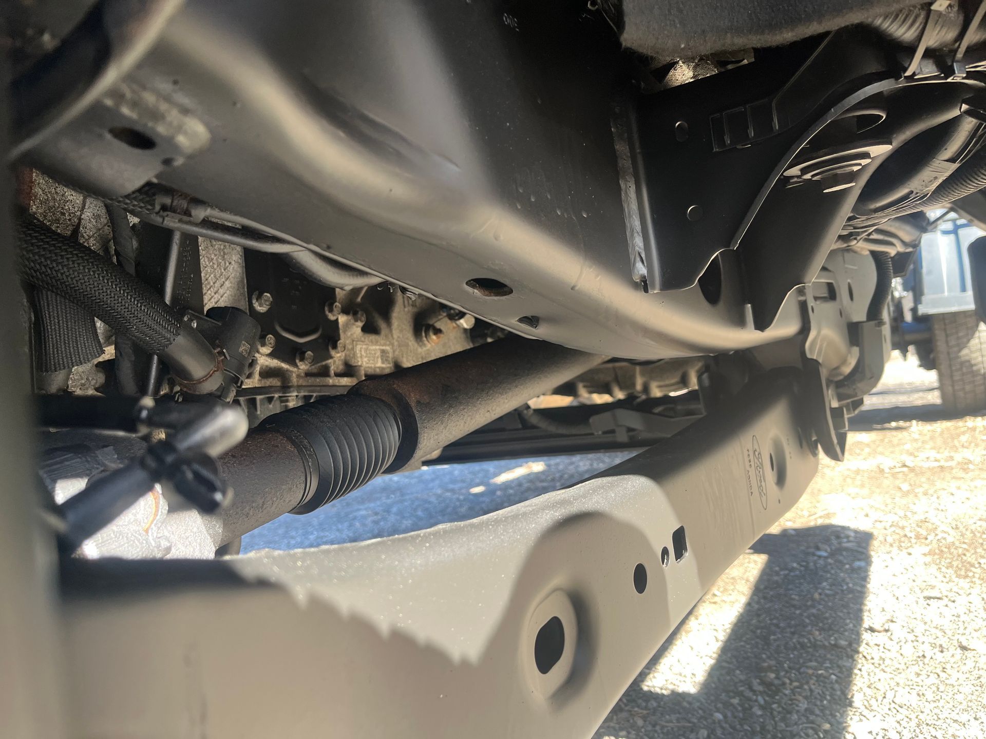 Underside of a vehicle showing the frame, steering components, and suspension, painted black and gray.