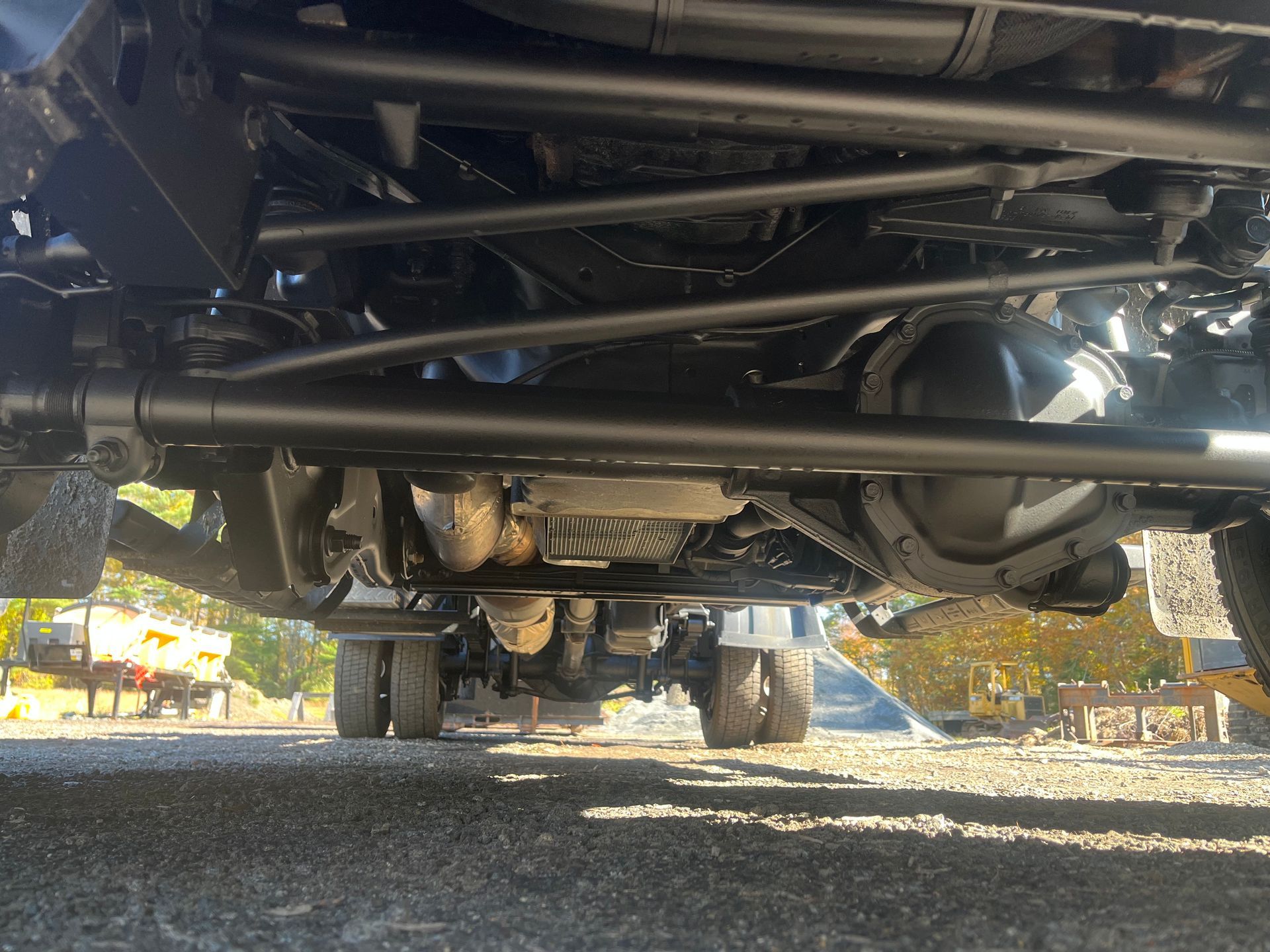 Underside view of a dark vehicle chassis, showing axles, suspension, and engine components.