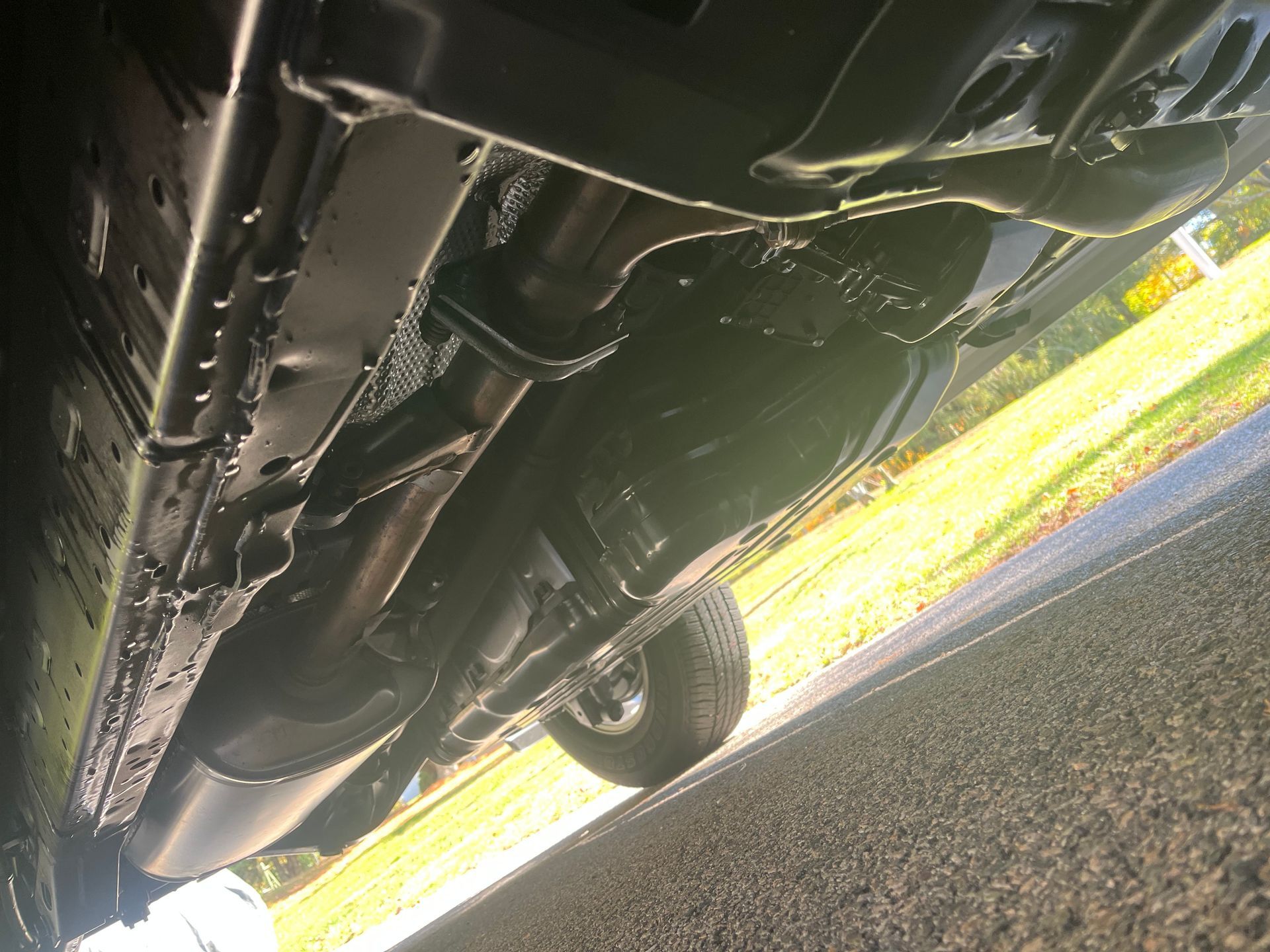 Underside of a black vehicle. Visible exhaust system, undercarriage details, and tire on asphalt.