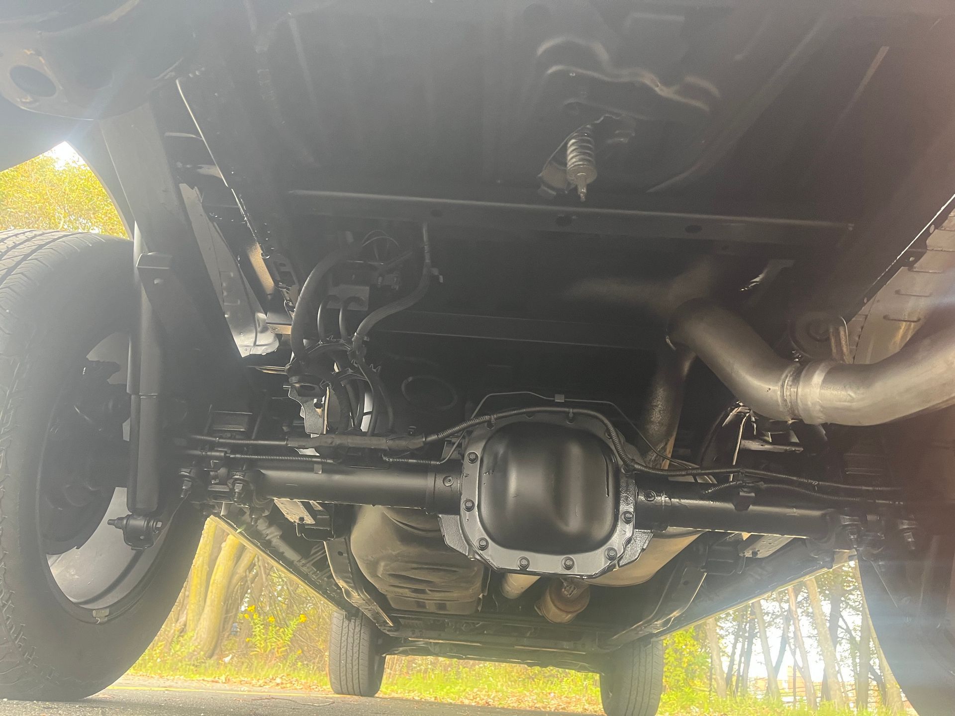 Undercarriage of a black truck, showing axle, exhaust, and suspension components, outdoors.
