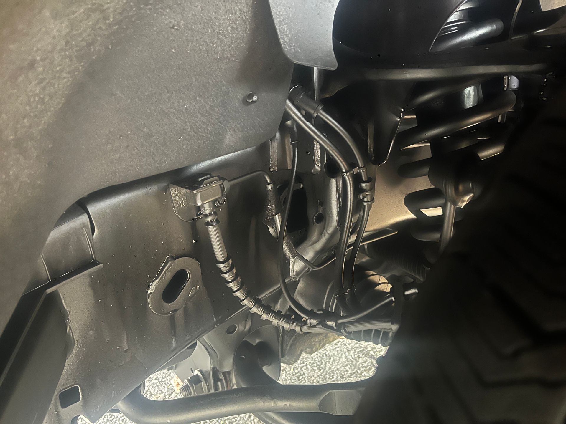 Undercarriage of a black truck, showing axle, exhaust, and suspension components, viewed from below.