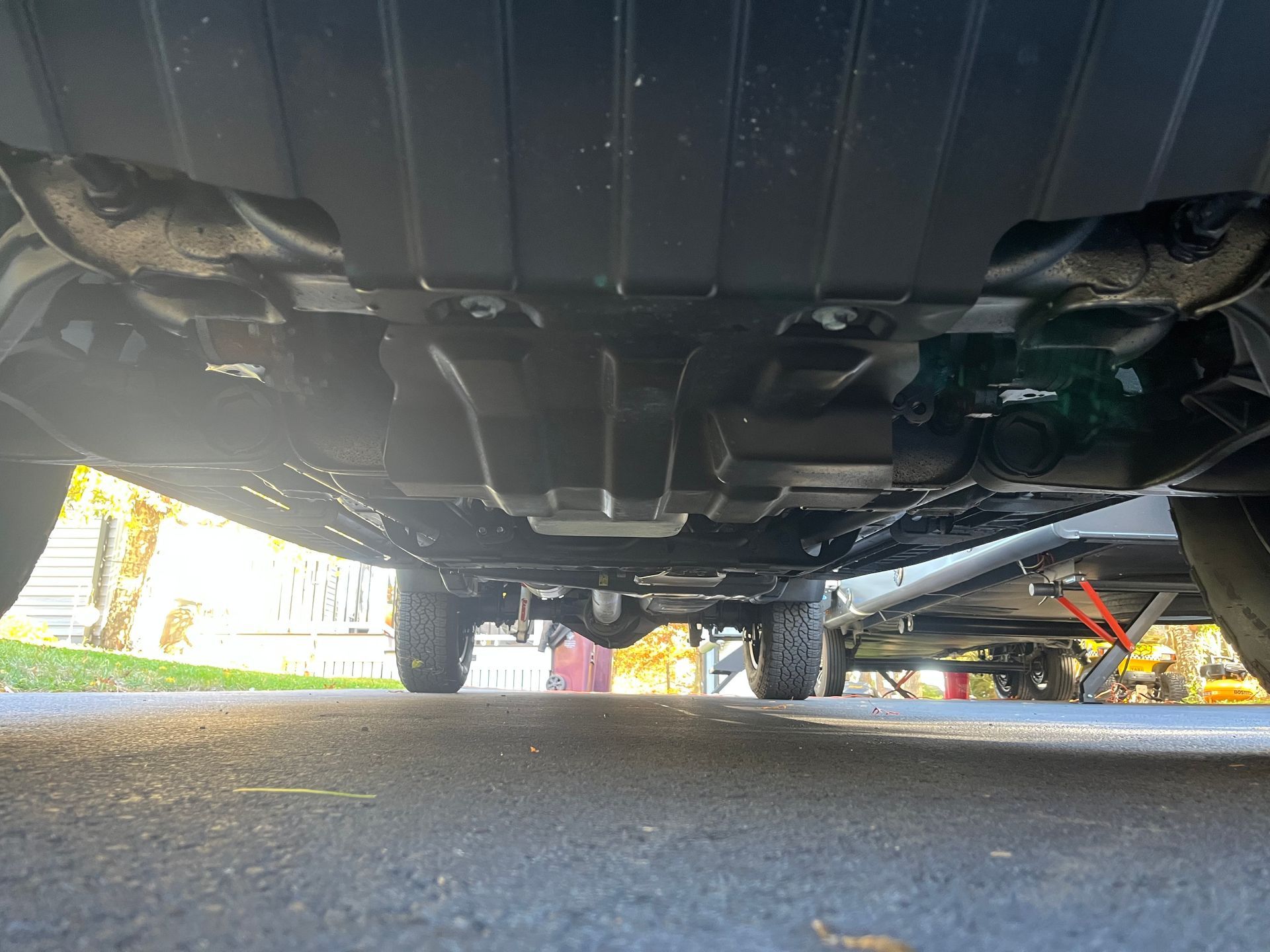 Underside of a vehicle on an asphalt driveway. Shows the undercarriage and wheels.