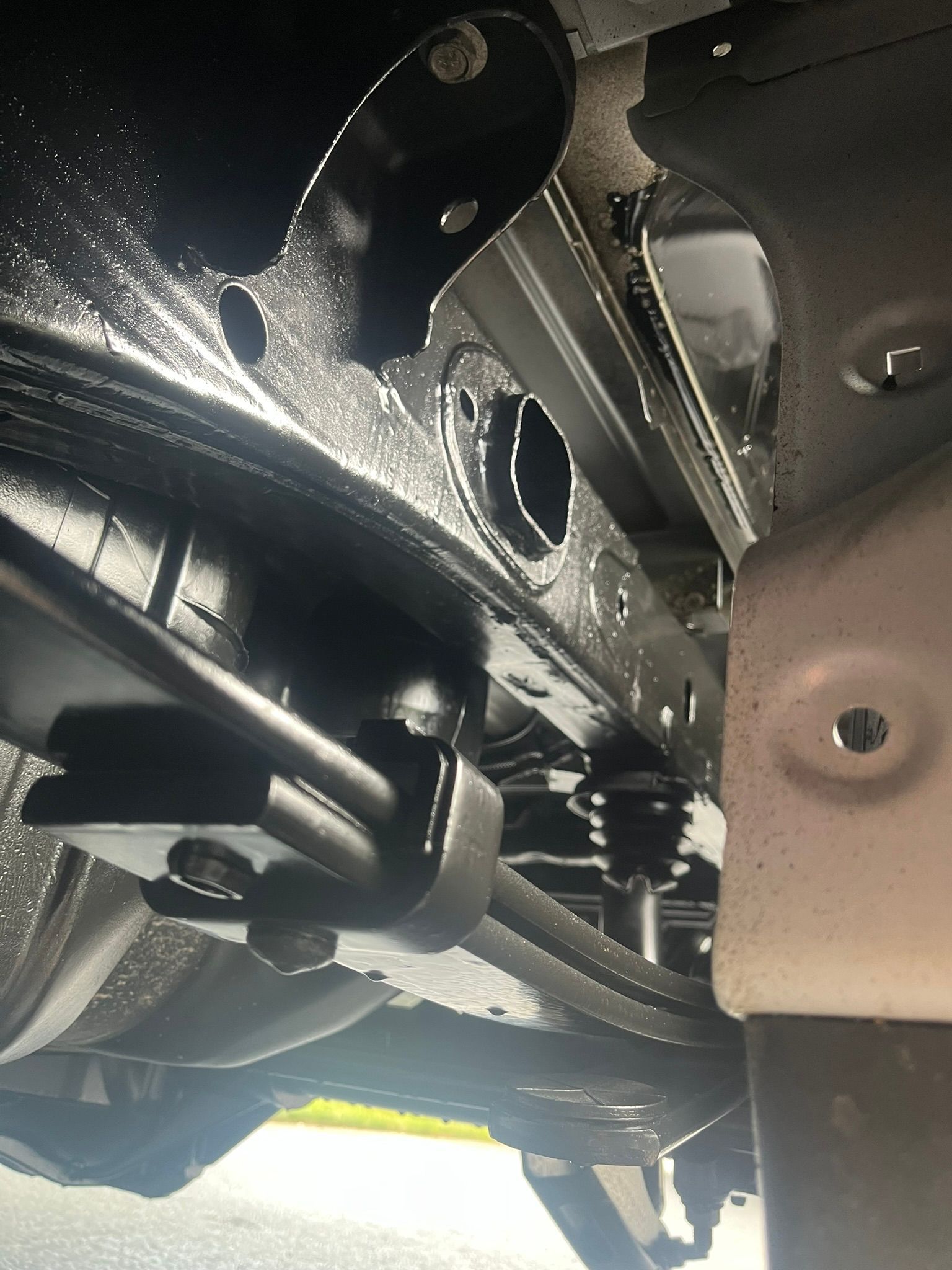 Underside view of a black car frame. Various parts and holes visible, painted in black and gray tones.