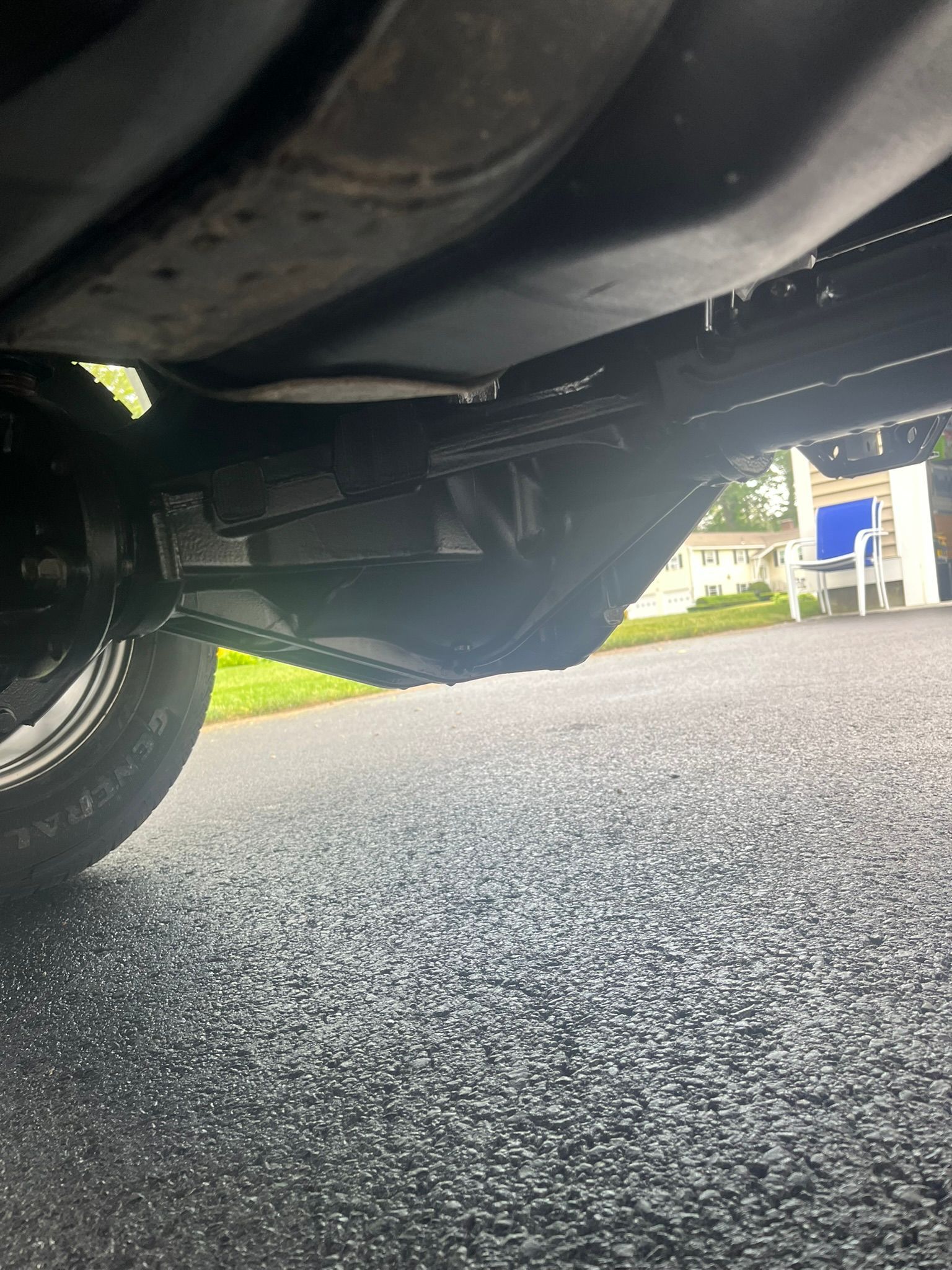 Underside view of a vehicle's dark chassis with a tire, on a wet asphalt road.