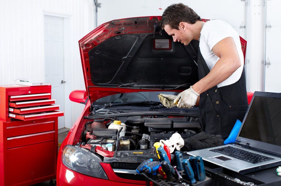 Mechanic working under the hood of a red car in an auto repair shop