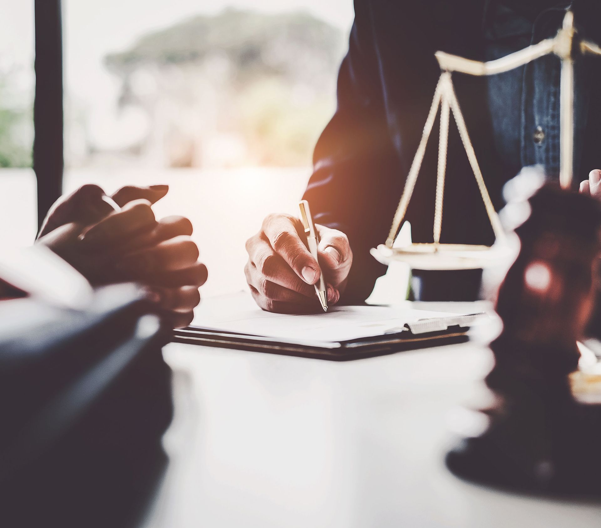 Learn More About Real Estate Hands signing documents at a desk, with a gavel and scales of justice in the background