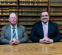 Two men in suits and ties are sitting at a table in front of a bookshelf