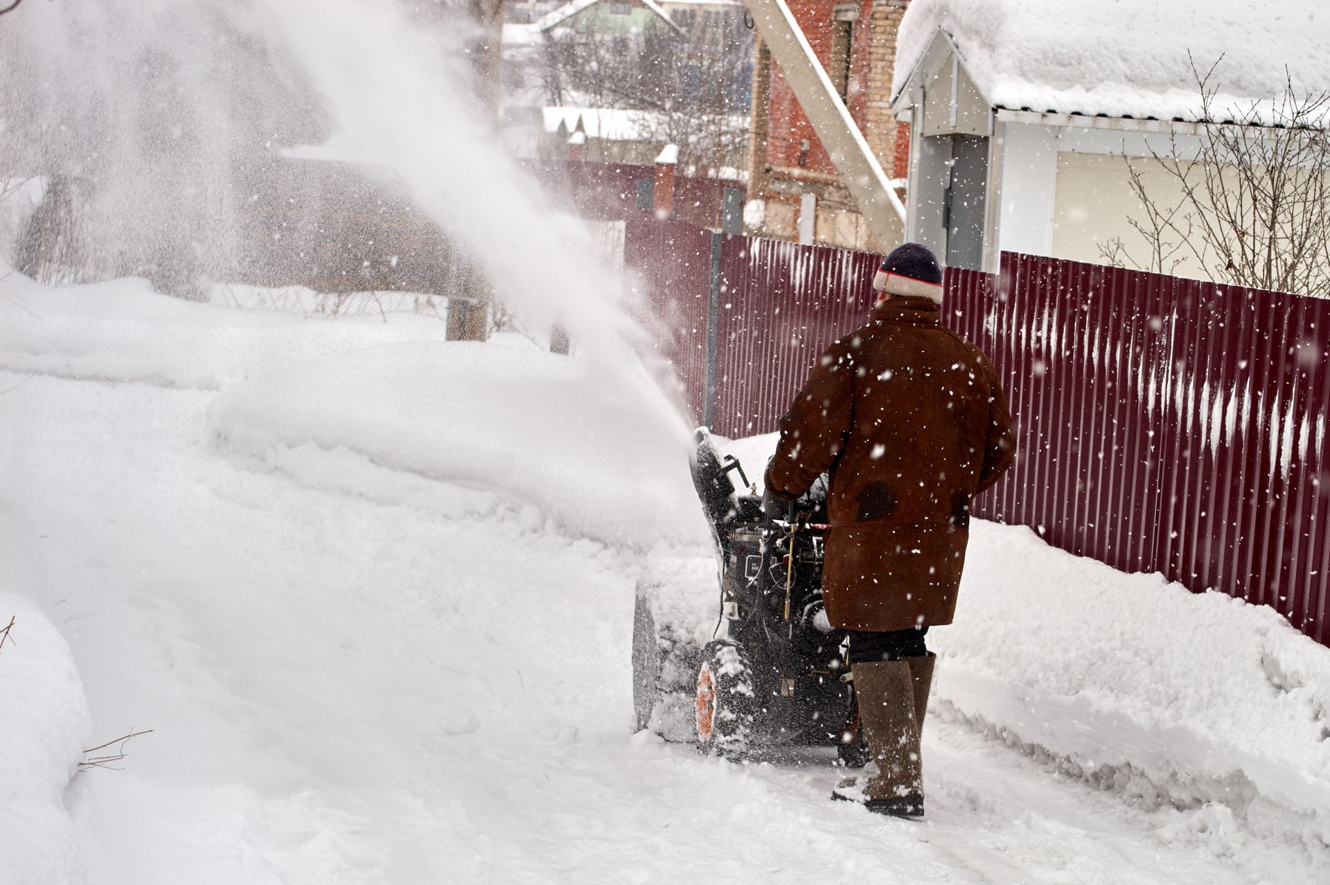 Person clearing snow with a snowblower beside a red fence on a snowy street