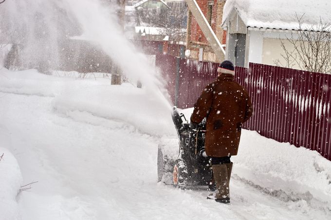 Person clearing snow with a snowblower beside a red fence on a snowy street