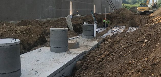 Construction site with concrete foundations and cylindrical columns in muddy dirt under overcast skies