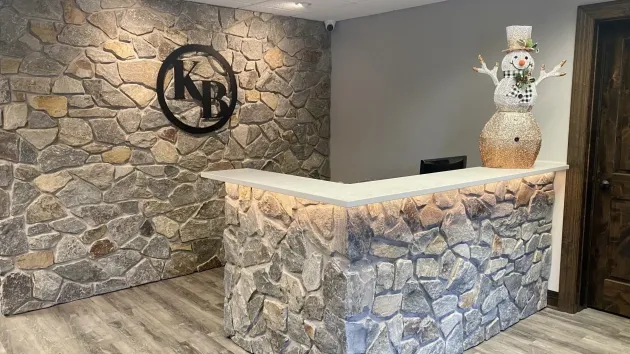 Stone-front reception desk in a modern lobby with gray walls, wood floor, and decorative flowers on top