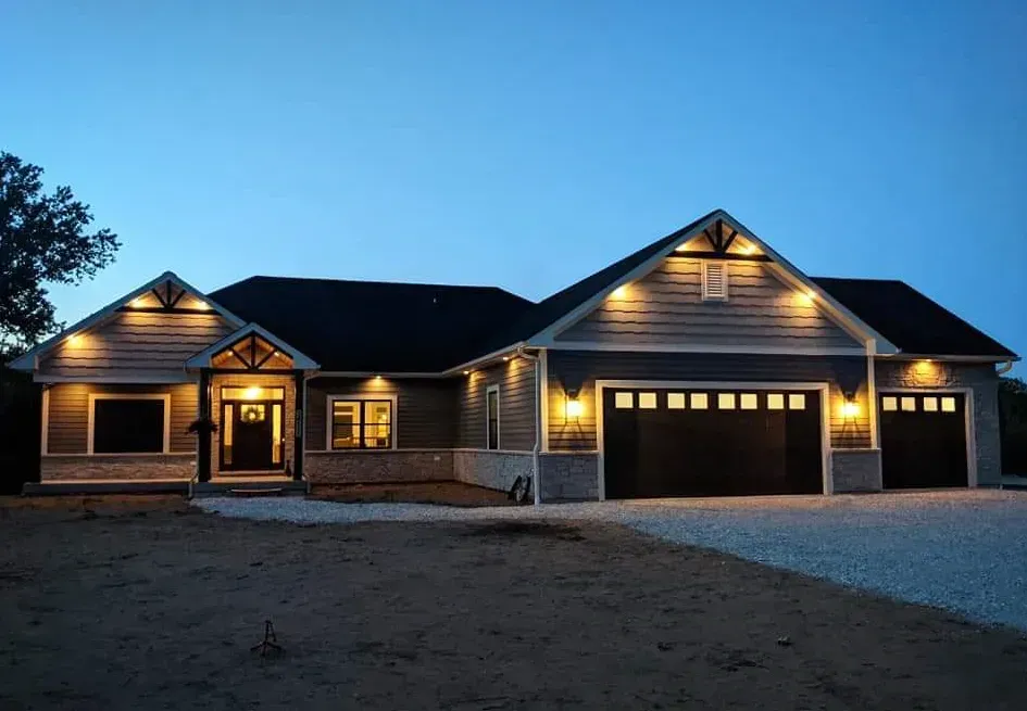 New suburban house at dusk with warm exterior lights and three garage doors
