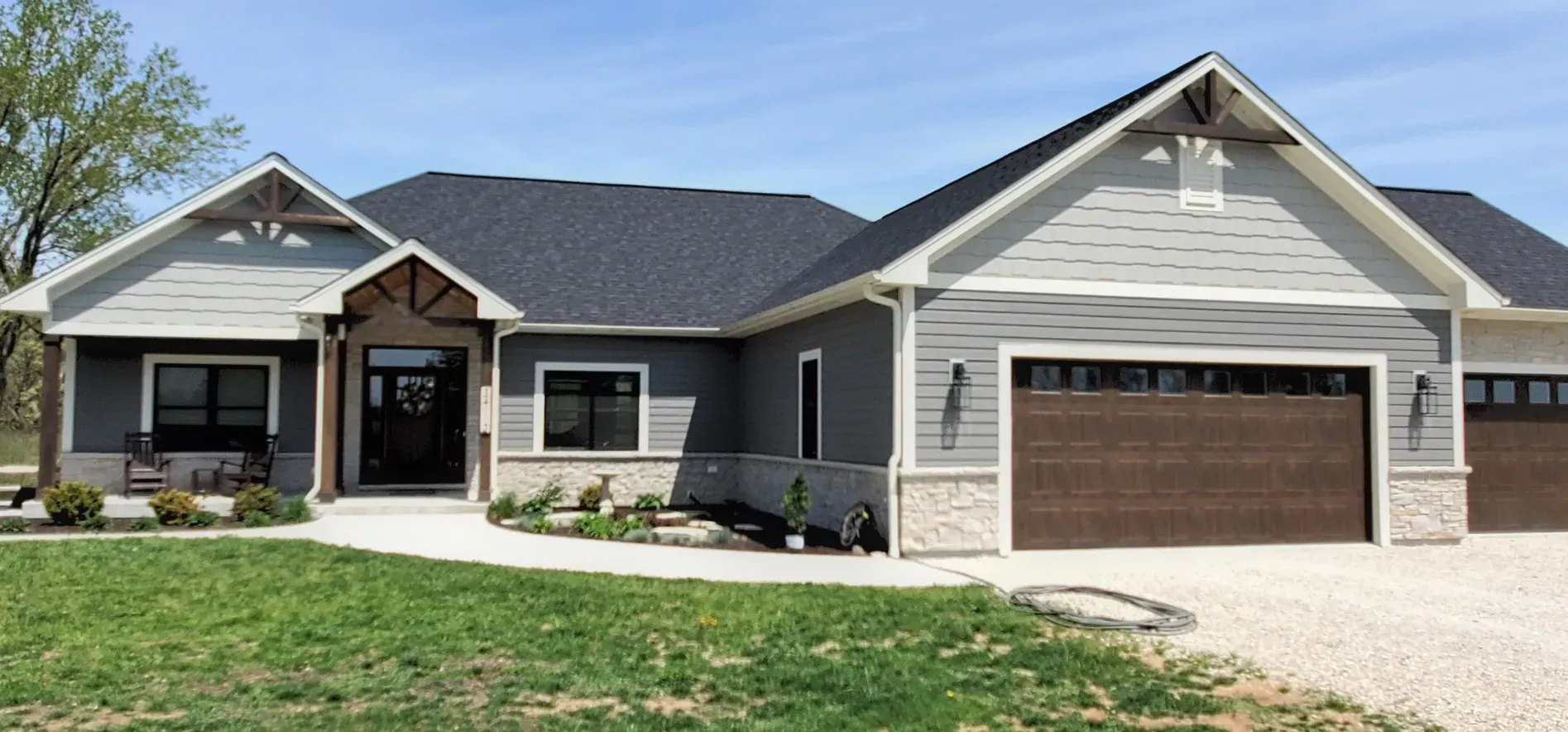 Modern single-story gray house with a front porch, gabled roof, and attached two-car garage