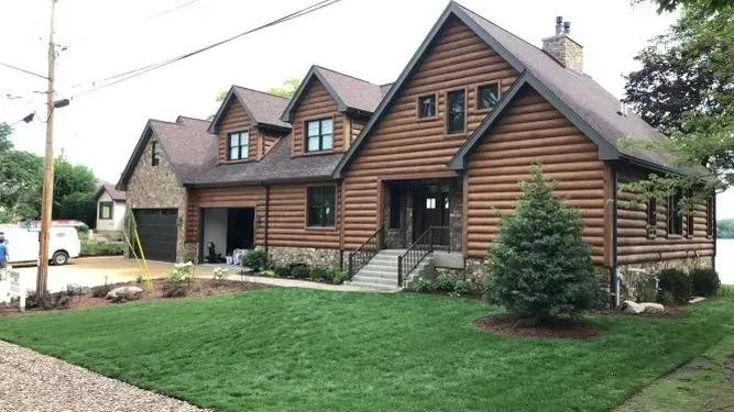 Log cabin-style house with brown wood siding, gabled roof, and a green lawn in front