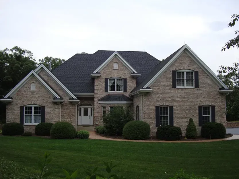 Large brick suburban house with a dark roof and manicured lawn