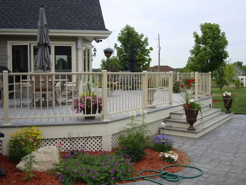 House deck with white railing, potted flowers, patio umbrella, and stone steps leading to a landscaped yard