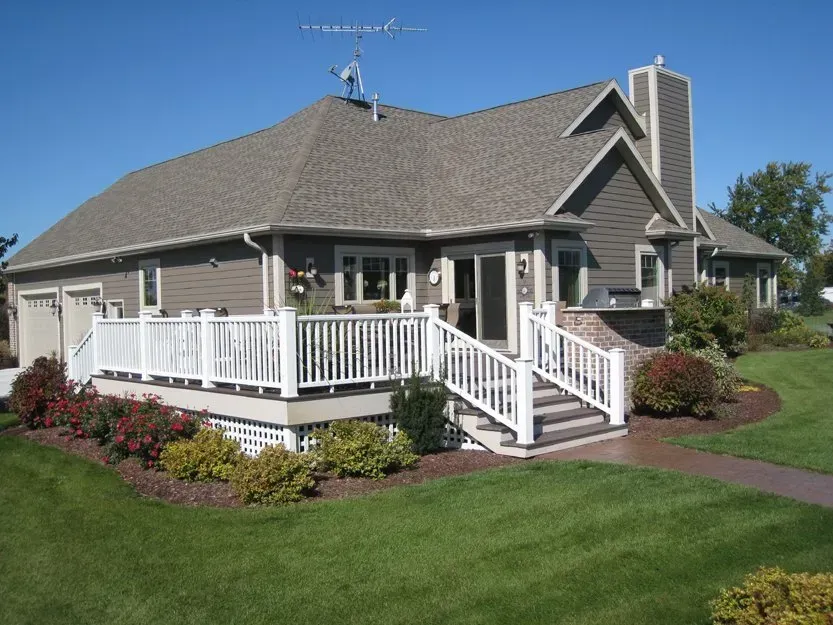 Suburban house with gray siding, white porch railing, and landscaped lawn under a clear sky