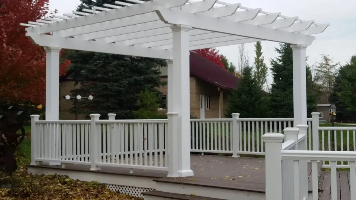 White pergola on a wooden deck with railing in a landscaped garden