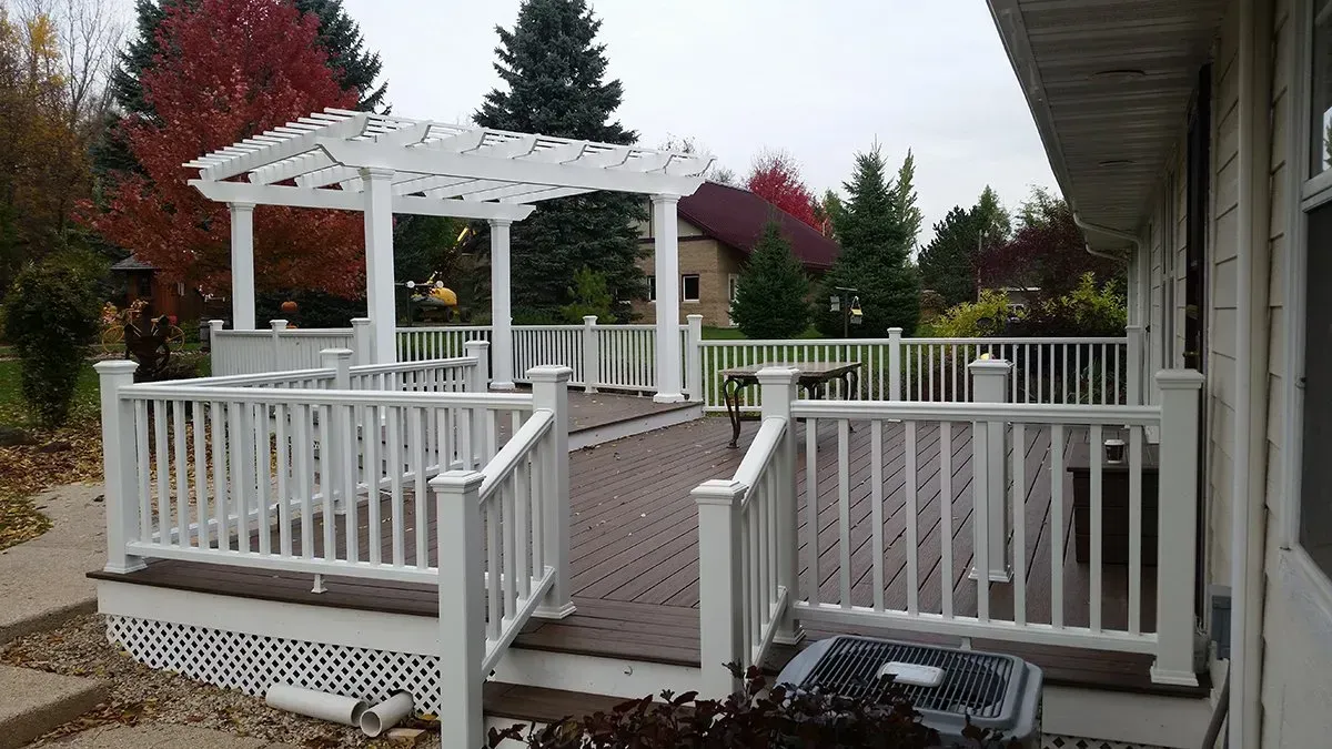 White deck with ramp and gazebo in a backyard, bordered by railings and autumn trees.