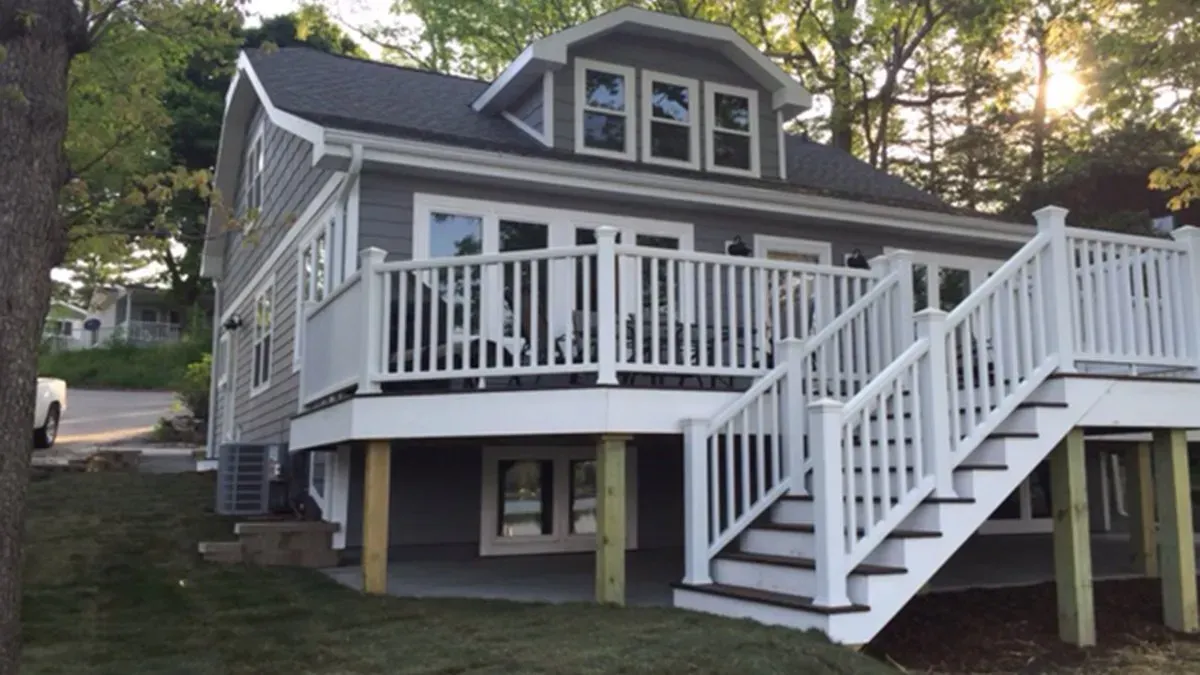 Gray house with white porch and stairs on a wooded hillside at dusk